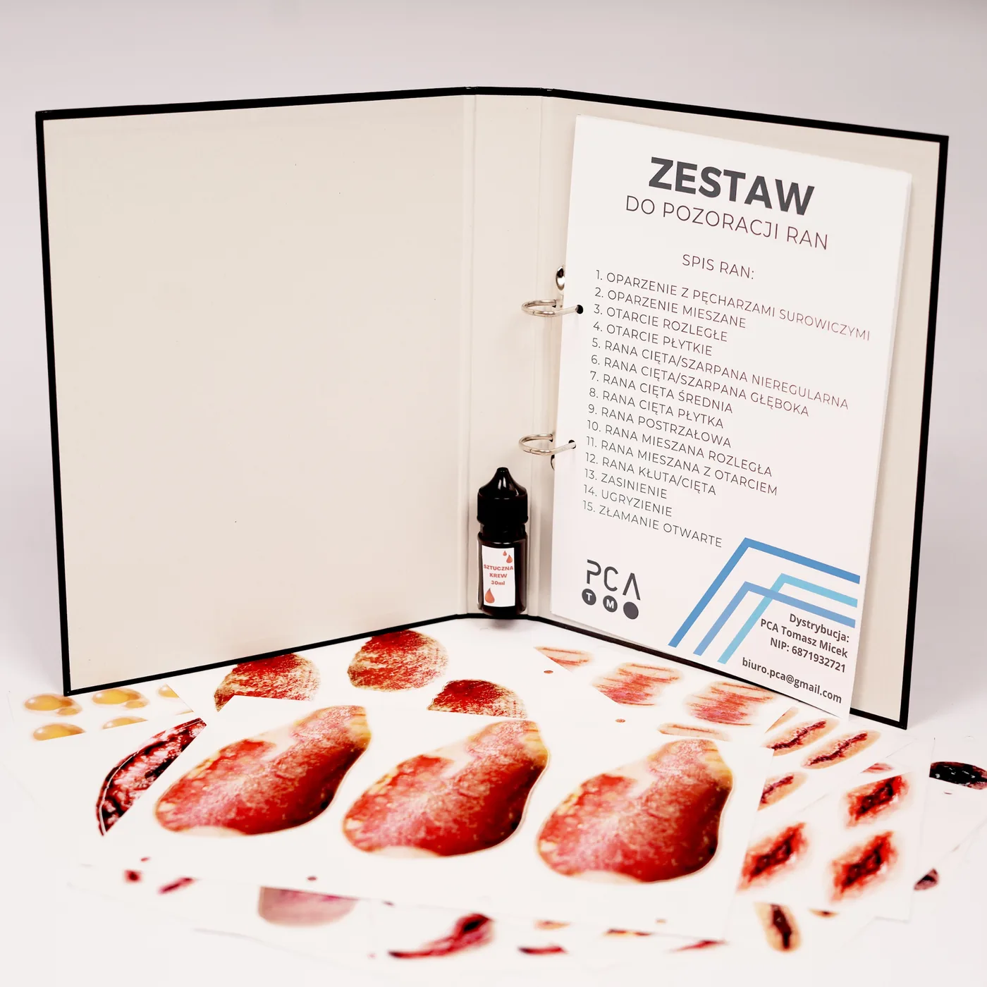 Otwarty segregator zestawu do pozoracji ran z arkuszami naklejek i sztuczną krwią